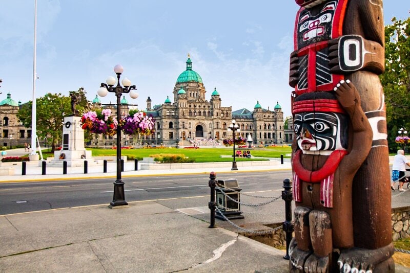 Das Parlamentsgebäude von British Columbia mit einem kunstvoll geschnitzten Totempfahl im Vordergrund.
