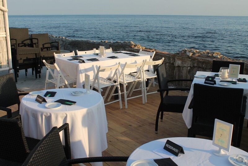 Reservierte Tische mit weißer Tischdecke in einem Restaurant am Meer in Málaga bei Sonnenuntergang