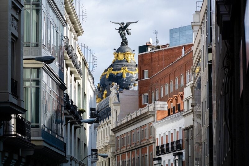 Historisches Metropolis-Gebäude mit goldverzierter Kuppel in Madrid, umgeben von klassischer und moderner Architektur.