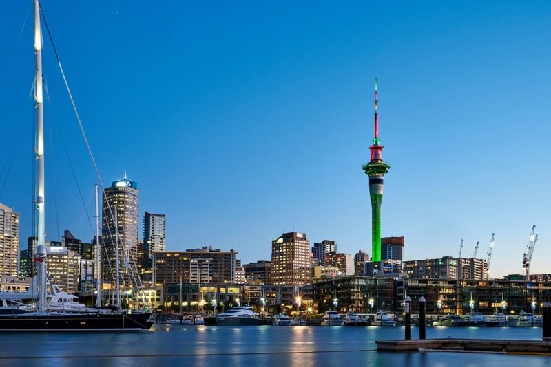 Skyline von Auckland bei Nacht mit beleuchtetem Sky Tower und Yachthafen.