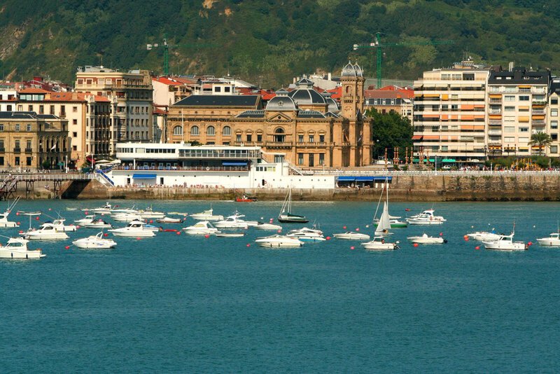 Historisches Rathaus von San Sebastián mit Yachten im Hafen und Stadtpanorama im Hintergrund