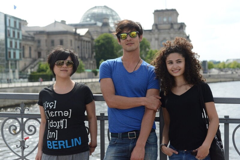 Drei junge Erwachsene posieren vor dem Berliner Reichstag an einem sonnigen Tag