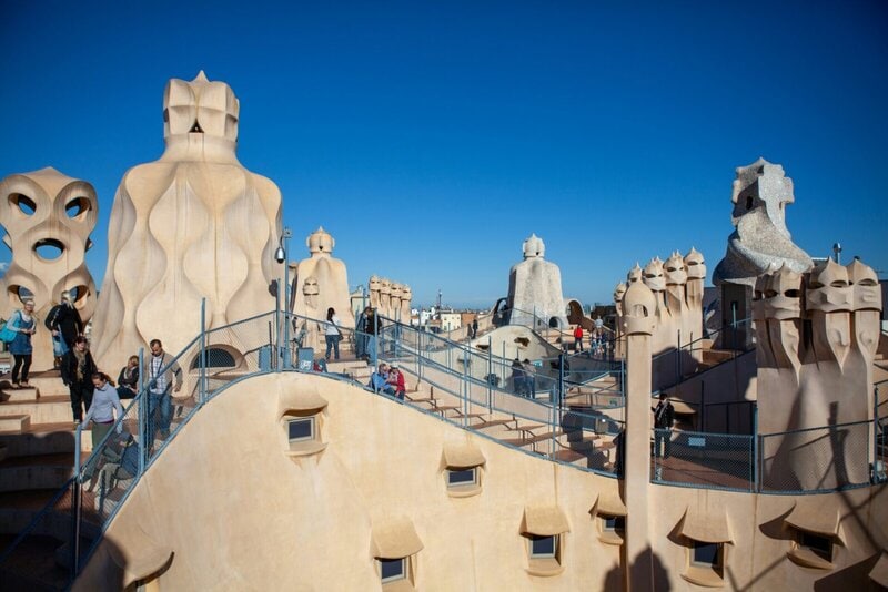 Das Dach von La Pedrera (Casa Milà) in Barcelona mit den markanten, skulpturalen Schornsteinen von Antoni Gaudí unter blauem Himmel.
