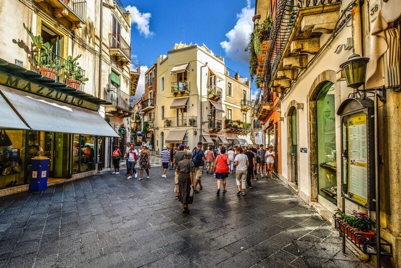 Belebte Altstadt von Taormina, Sizilien, mit historischen Gebäuden, Balkonen und geschäftigen Straßen voller Touristen.