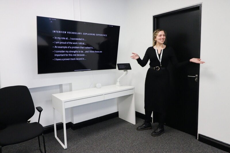 Mitarbeiterin hält eine Präsentation über Interview-Vokabular in einem modernen Besprechungsraum mit Bildschirm und Whiteboard.