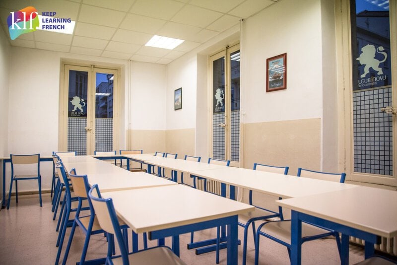 Heller und moderner Klassenraum der Sprachschule Lyon Bleu International mit blauen Stühlen und weißen Tischen.