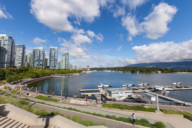 Panoramablick auf Vancouver Harbour mit modernen Hochhäusern, Wasserflugzeugen und dem Stanley Park im Hintergrund.