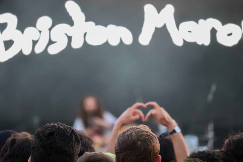 A fan holds up a heart with their fingers with "Briston Maroney" on the screen in the background