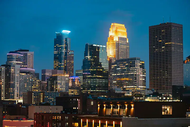 Downtown Minneapolis skyline illuminated at twilight, featuring the glowing Capella Tower and skyscrapers representing Twin Cities web design agencies.
