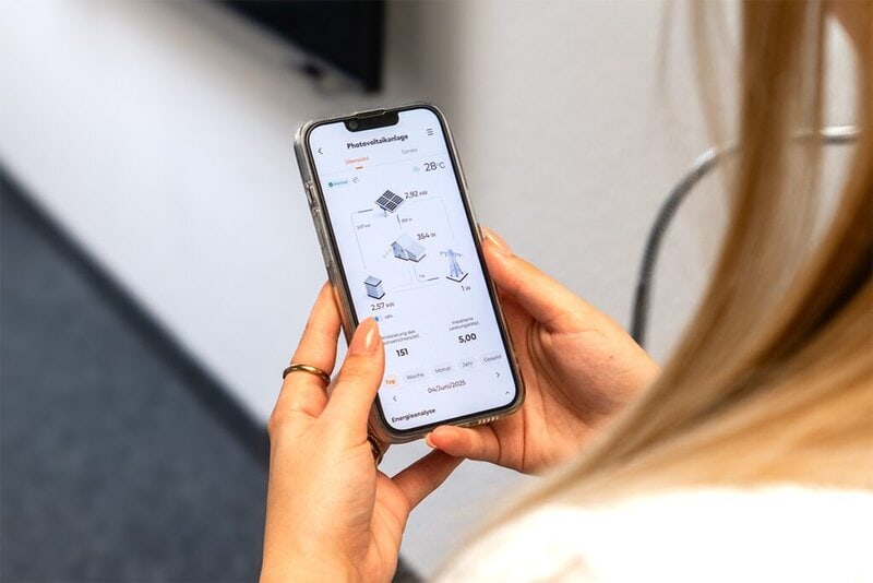 Abbildung einer Person mit Smartphone in der Hand. Auf dem Smartphone ist die Energie-App der PV-Anlage abgebildet.