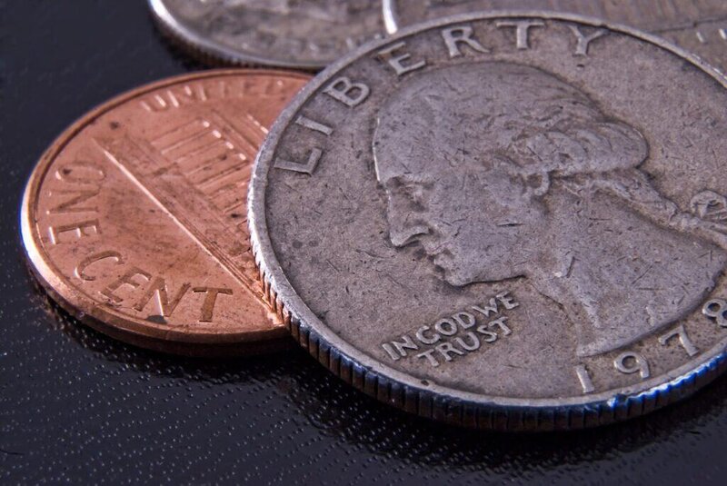 Close-up of US coins, including a quarter and a penny, on a dark surface.