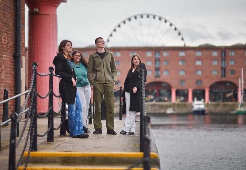 Junge Menschen genießen die Aussicht am Albert Dock in Liverpool mit dem Riesenrad im Hintergrund.