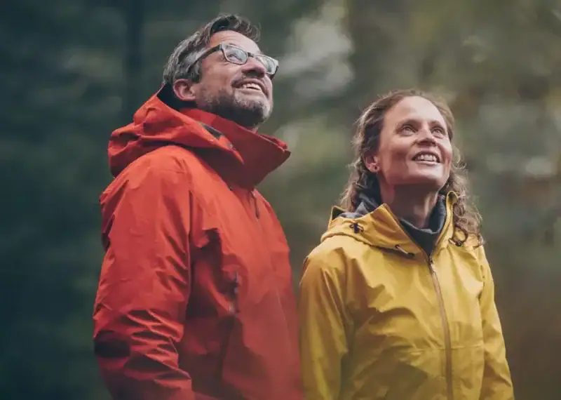 Matrimonio de 55 años sonrientes observando el paisaje mientras hacen trecking por la montaña