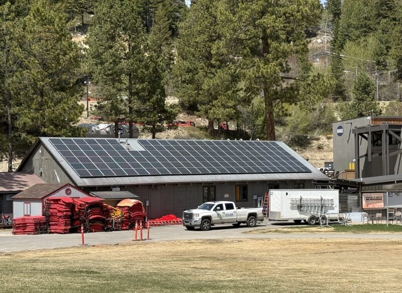Solar panels on the roof of Bogus Basin's rental shop, with a truck and trailer out front that have EGT Solar logo on them, and pine trees behind the building