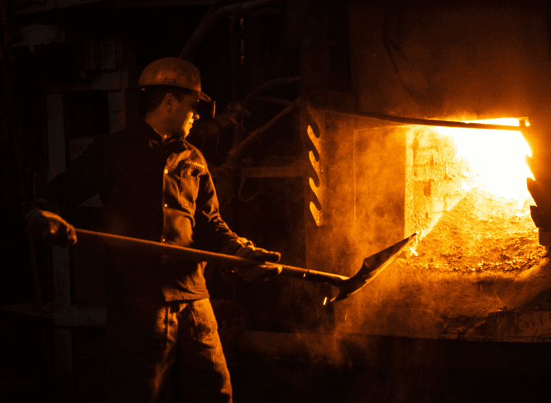 Arbeiter an einem Gießerei-Ofen, der Metallstaub und Hitze ausgesetzt ist, was die Notwendigkeit einer Staubüberwachung durch Dustlight bei Feinstaubbelastungen unterstreicht.