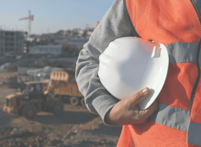 Mitarbeiter der Bauindustrie auf einer Baustelle mit Schutzhelm und Warnweste vor schwerem Baugerät.