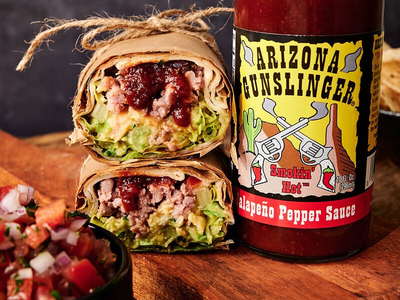 Burrito plate on a table with a bottle of AZ Gunslinger Red Jalapeño hot sauce beside it