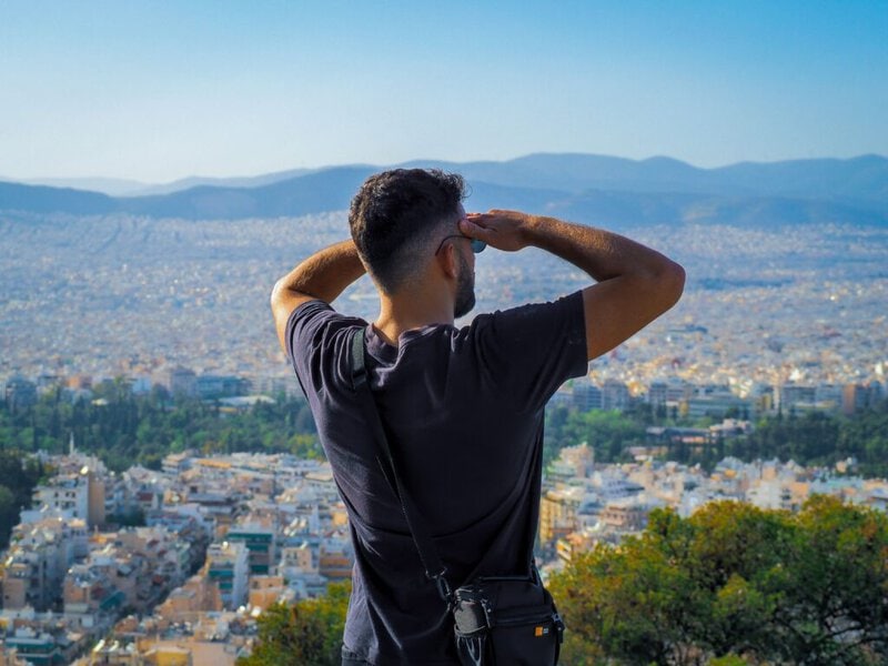 A man in a black shirt surveys a sprawling cityscape from a picturesque hilltop view.