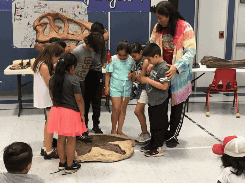 Dinosaurs Rock School Assembly in California Group of students comparing the size of their foot to a T-Rex Footprint