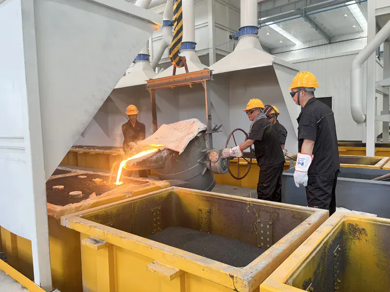 Workers pouring molten metal into a casting flask under extraction ducts