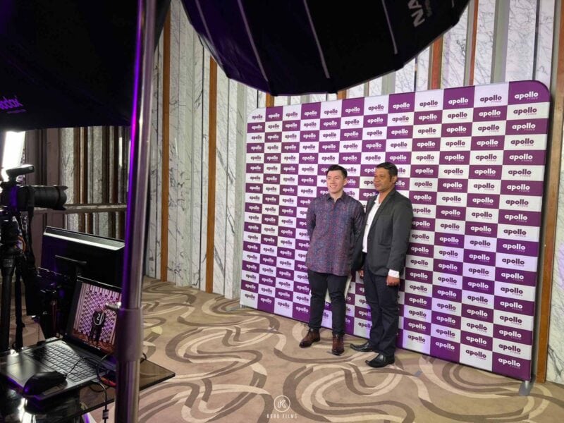 Two guests in suits posing in front of the logo backdrop at a magnet photo booth