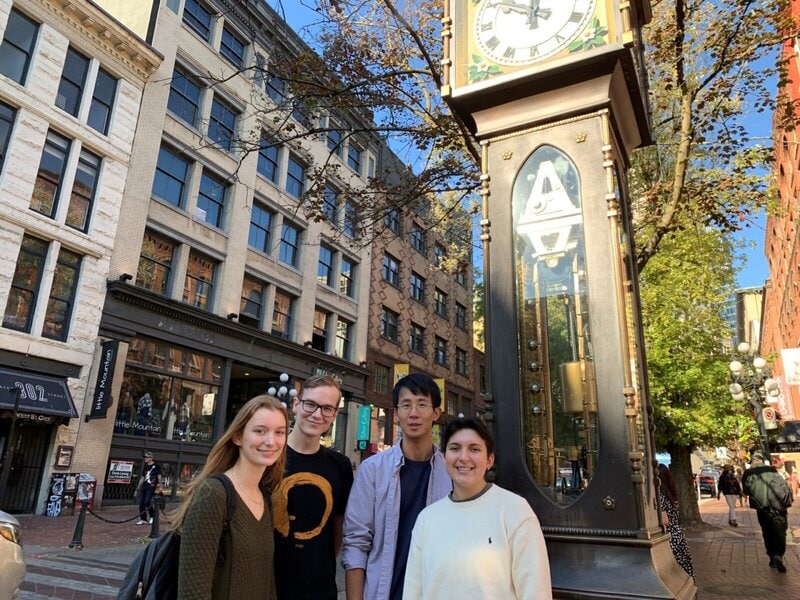 Gruppe junger Menschen vor der berühmten Steam Clock in Gastown, Vancouver, mit historischen Gebäuden im Hintergrund.