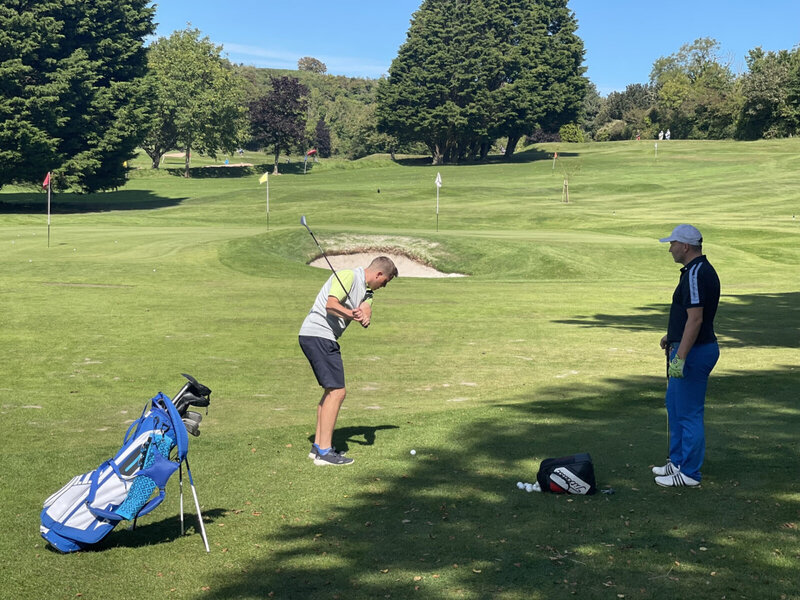 Golfspieler beim Training auf einem gepflegten Golfplatz mit grünen Fairways und Fahnenmarkierungen.