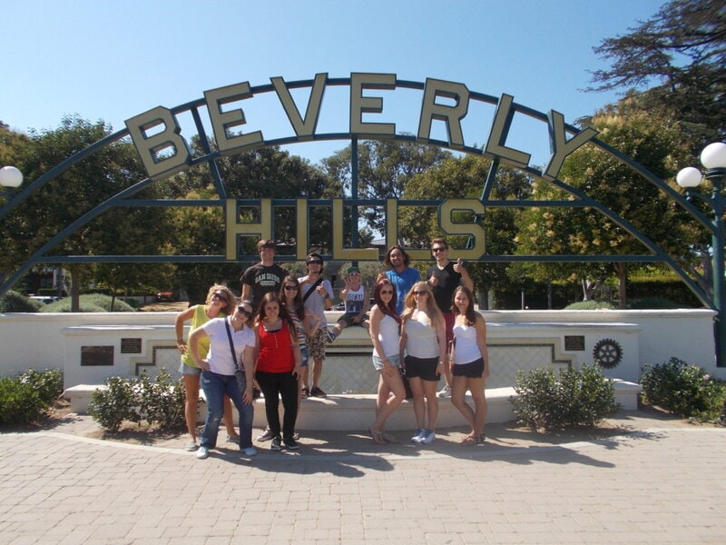 Eine Gruppe junger Menschen posiert vor dem berühmten „Beverly Hills“-Schild in Los Angeles, Kalifornien, an einem sonnigen Tag.
