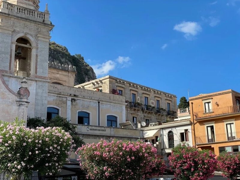Historische Architektur in einer mediterranen Stadt mit blühenden Oleanderbüschen unter blauem Himmel.
