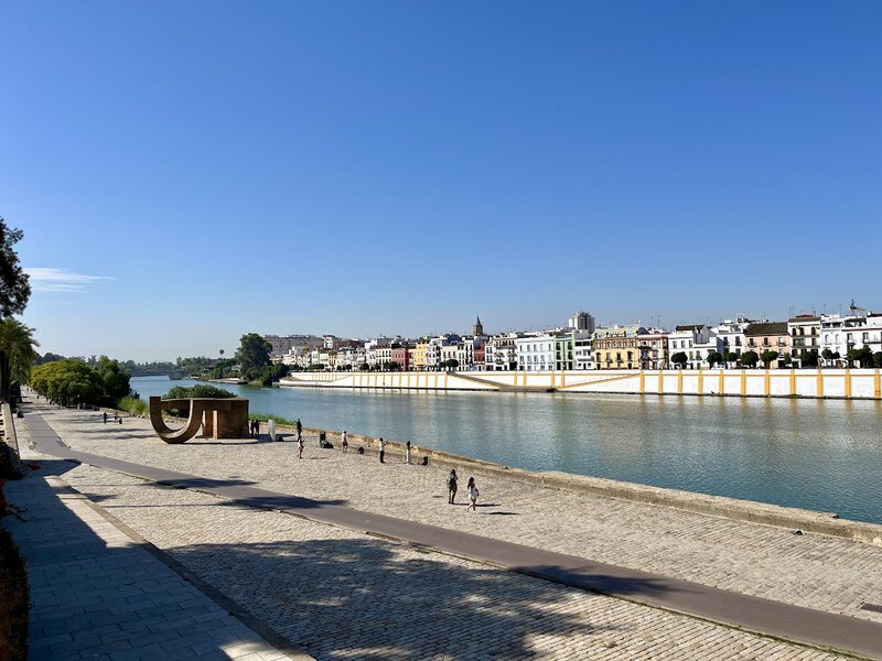 Blick auf das Flussufer des Guadalquivir mit dem Stadtteil Triana in Sevilla bei klarem, blauem Himmel.