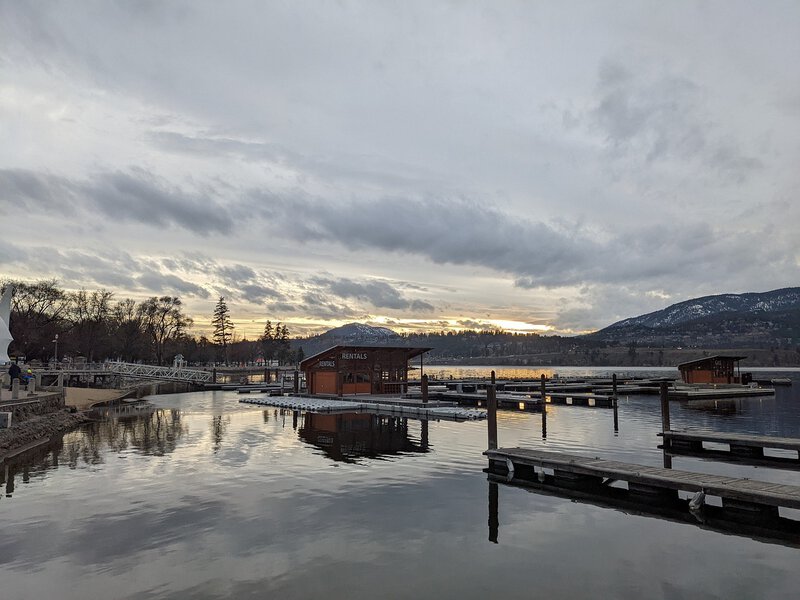 Idyllischer Hafen bei Sonnenuntergang mit ruhigem Wasser, Bootsanlegern und malerischer Bergkulisse im Hintergrund.