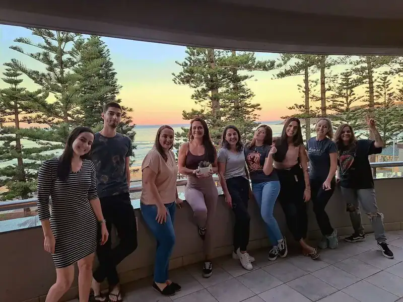 Gruppe junger Menschen genießt den Sonnenuntergang auf einem Balkon mit Blick auf den Ozean.