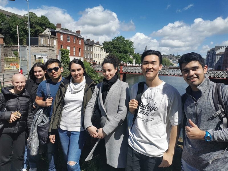 Internationale Sprachschüler in Cork, Irland, mit einer Brücke und der Stadt im Hintergrund.