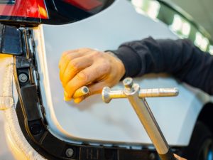 Technician repairing large dents on a car using specialist tools.