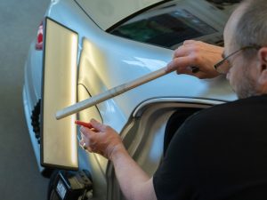 a man repairing a car by using techniques to get the dent out of car easily