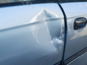 A close-up of a car door with a dent, demonstrating the process of removing small dents from a car.