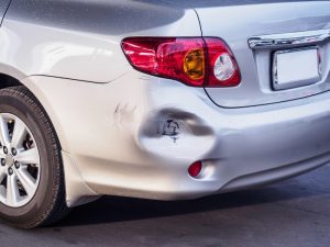 Close-up of a large dent on a silver car, highlighting the need for small dent auto repair.