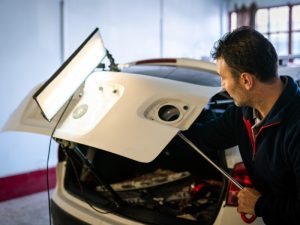 Technician performing dent repair in car boot using specialised tools and light board