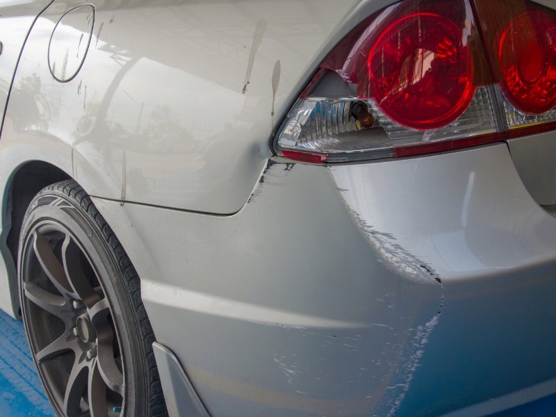 Rear car panel showing chips and dents around the bumper and tail light area.