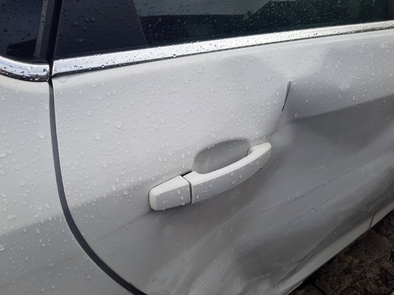 Wet white car door showing a shallow dent near the handle, illustrating cost to remove car dents.