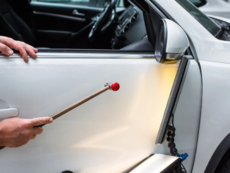 Paintless dent removal tool in use, demonstrating repair methods that affect cost to remove car dents.