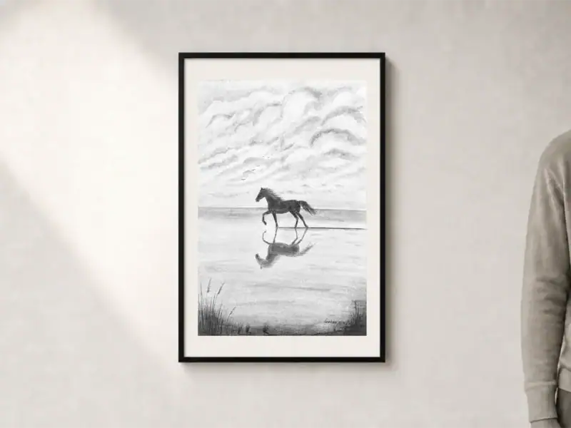 Disegno in carboncino di un cavallo libero che corre sulla battigia, con il riflesso nell’acqua lasciata dall’onda appena ritirata, uccelli e cielo nuvoloso sullo sfondo; passepartout e cornice nera, dimensioni esterne 52 × 72 cm.