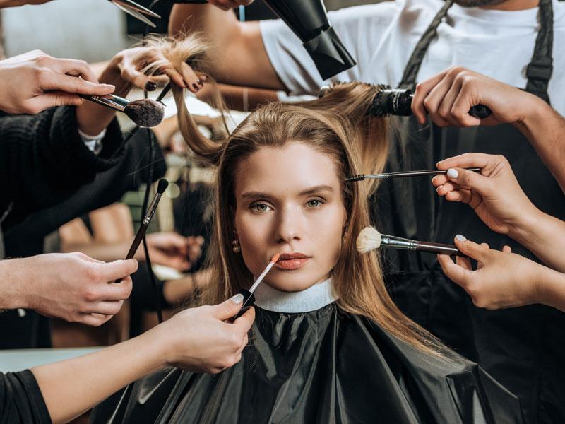 Model surrounded by cosmetologists with makeup and hair brushes