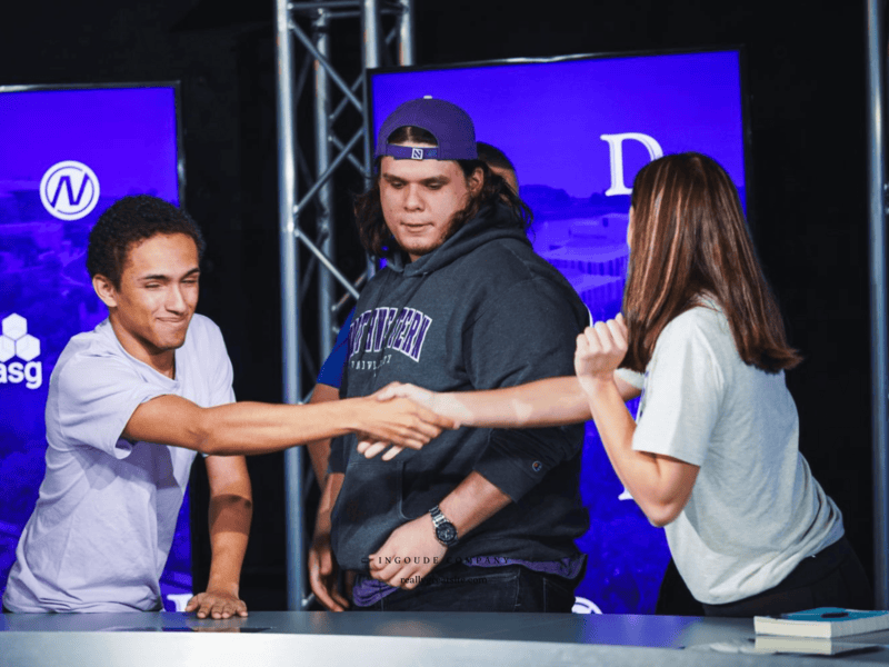 two people shake hands, one person watches handshake