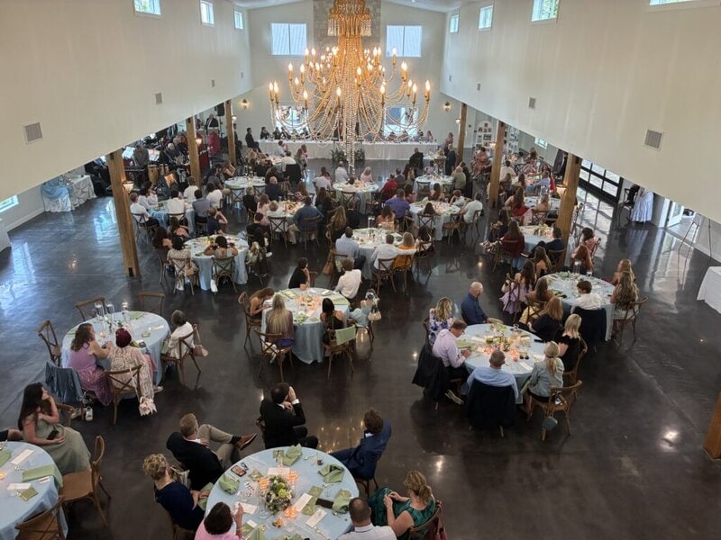 Aerial view of a wedding reception in the hall with guests seated at tables under a lit chandelier