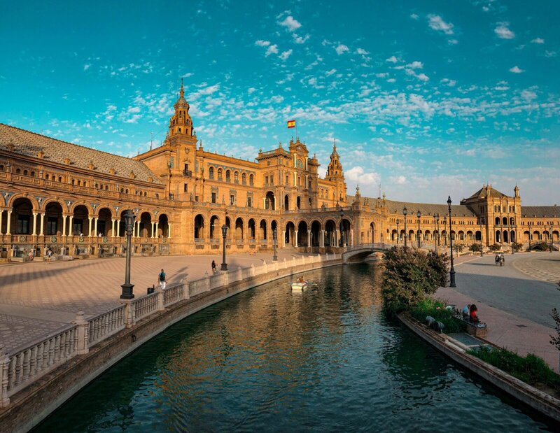 Panoramablick auf die Plaza de España in Sevilla mit Wasserkanal, Brücken und beeindruckender historischer Architektur bei Sonnenuntergang.