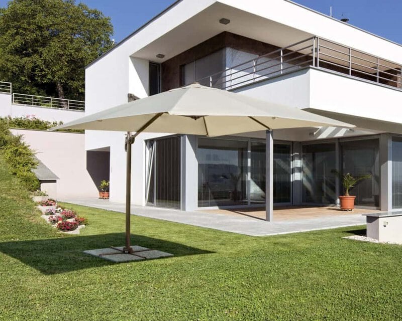 Ombrellone di design su terrazza di casa moderna con giardino curato.