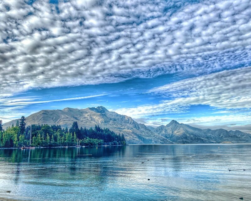 Spektakuläre Aussicht auf den Lake Wakatipu in Queenstown, Neuseeland, mit ruhigem Wasser, Bergen im Hintergrund und einer beeindruckenden Wolkenformation am Himmel.