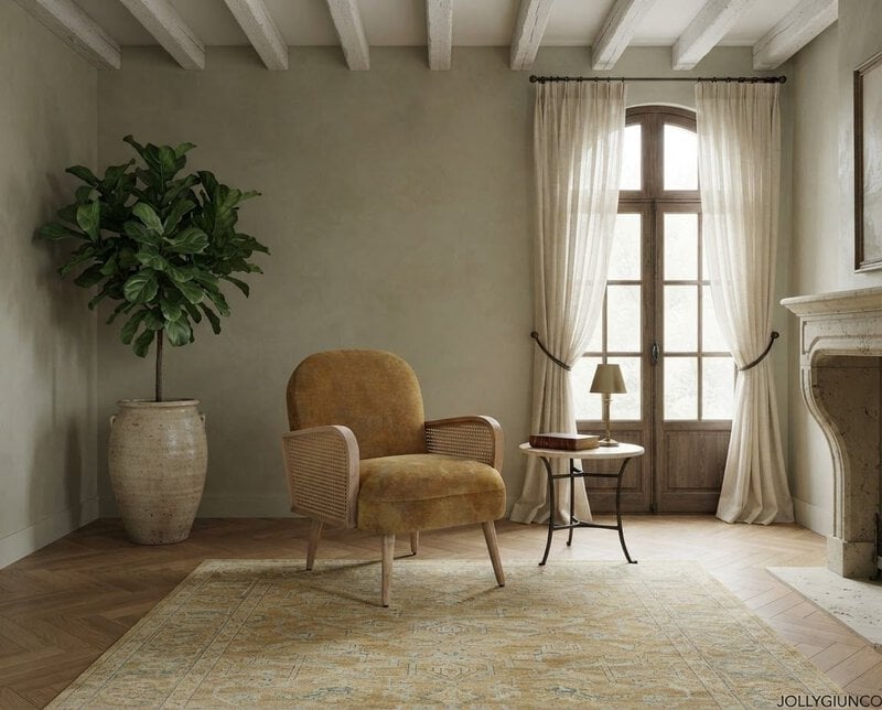 Cozy living room corner with a mustard armchair, side table, lamp, and large potted plant near a window with sheer curtains.