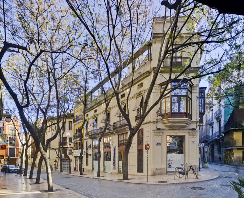 Historisches Eckgebäude in mediterraner Altstadt mit Bäumen und Kopfsteinpflaster